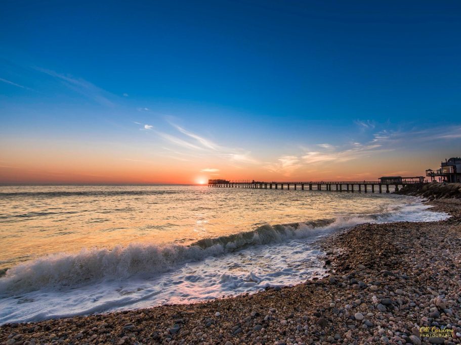 Sonnenuntergang über dem Meer, sanfte Wellen treffen auf den Kiesstrand.