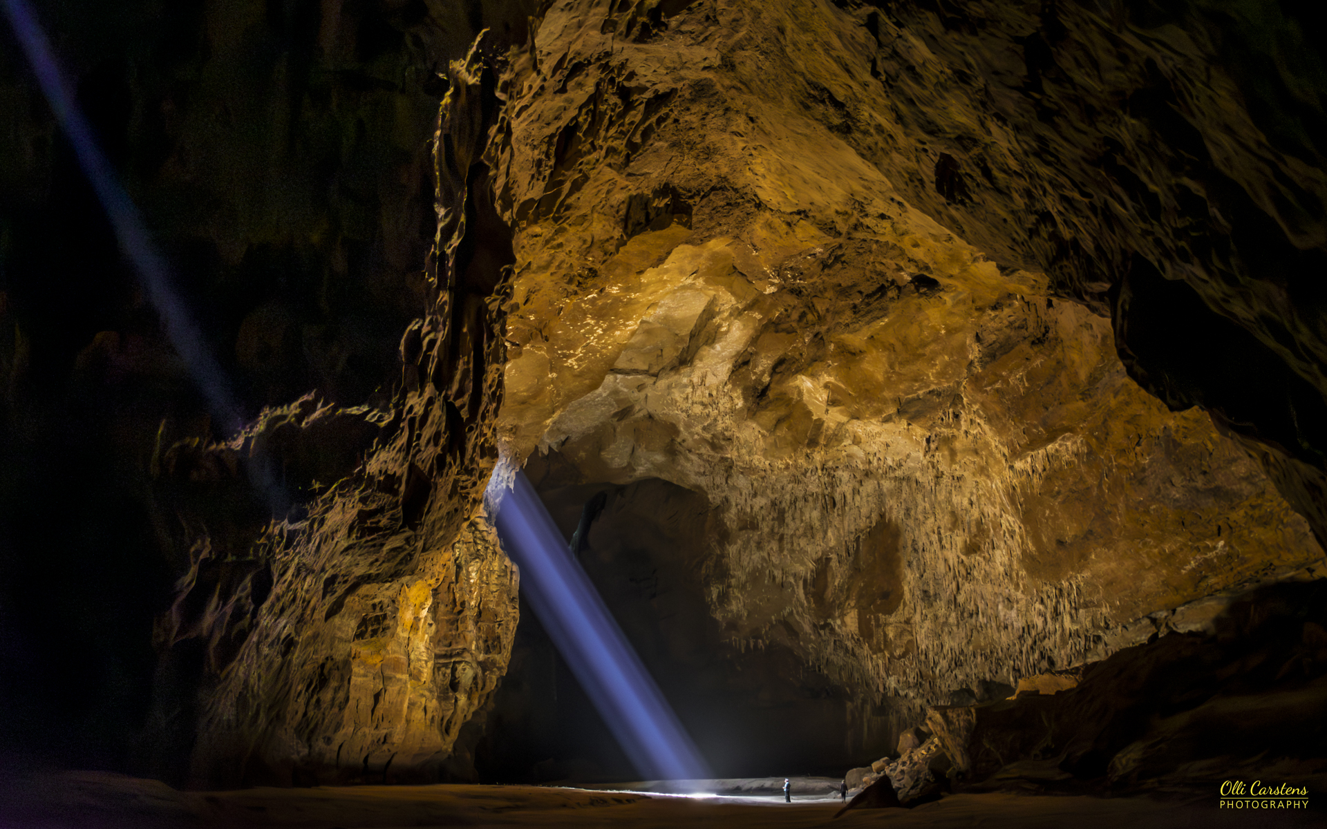 Unbekannte Destinationen mit Buschmann Safaris in Angola besuchen. Lichtstrahlen fallen in eine dunkle Höhle mit goldenen Felswänden.