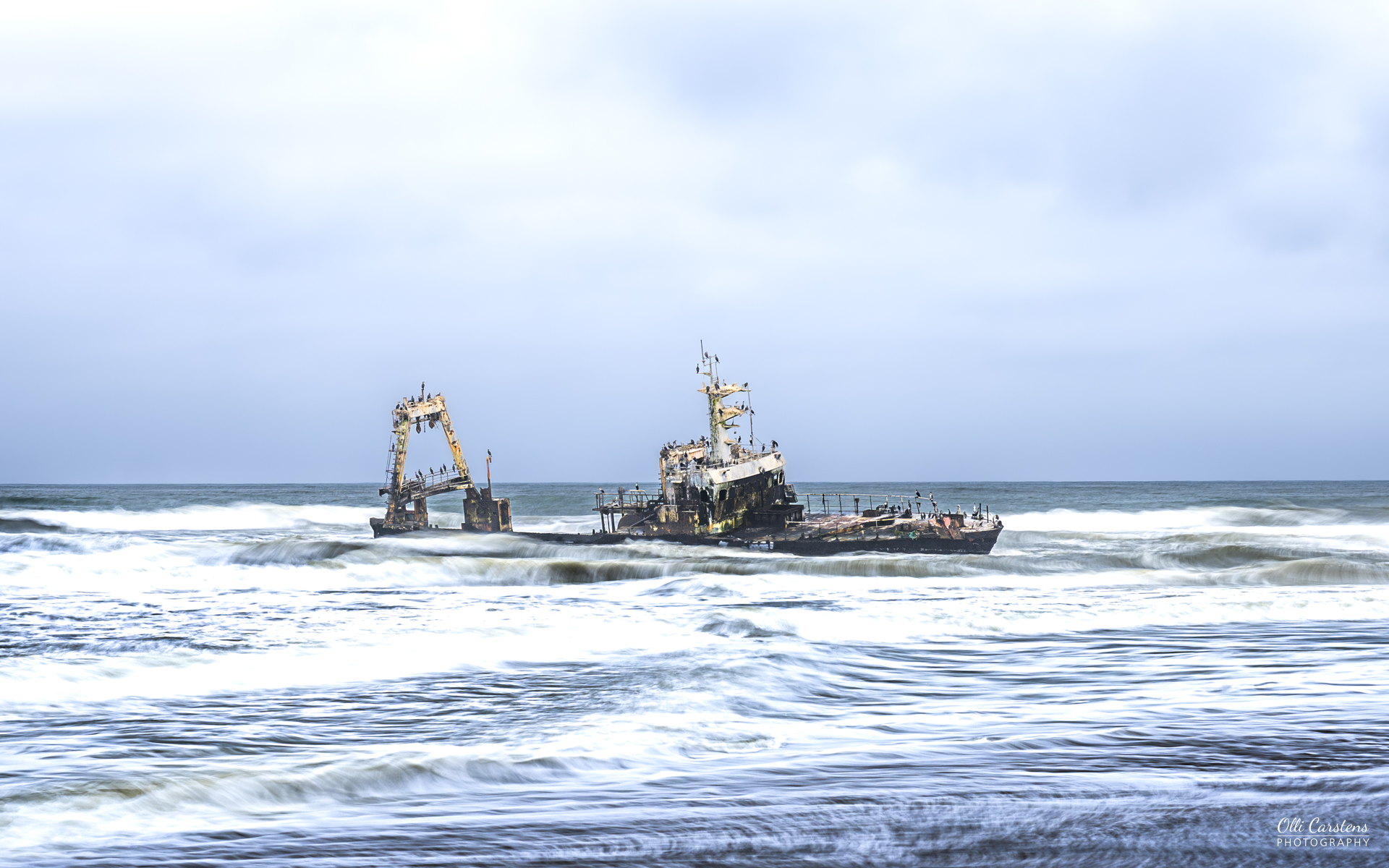 Langzeitbelichtung der „Zeila“ in der Brandung. Fotosafari in Namibia Ein gestrandetes Schiff im Welter mit stürmischem Himmel.