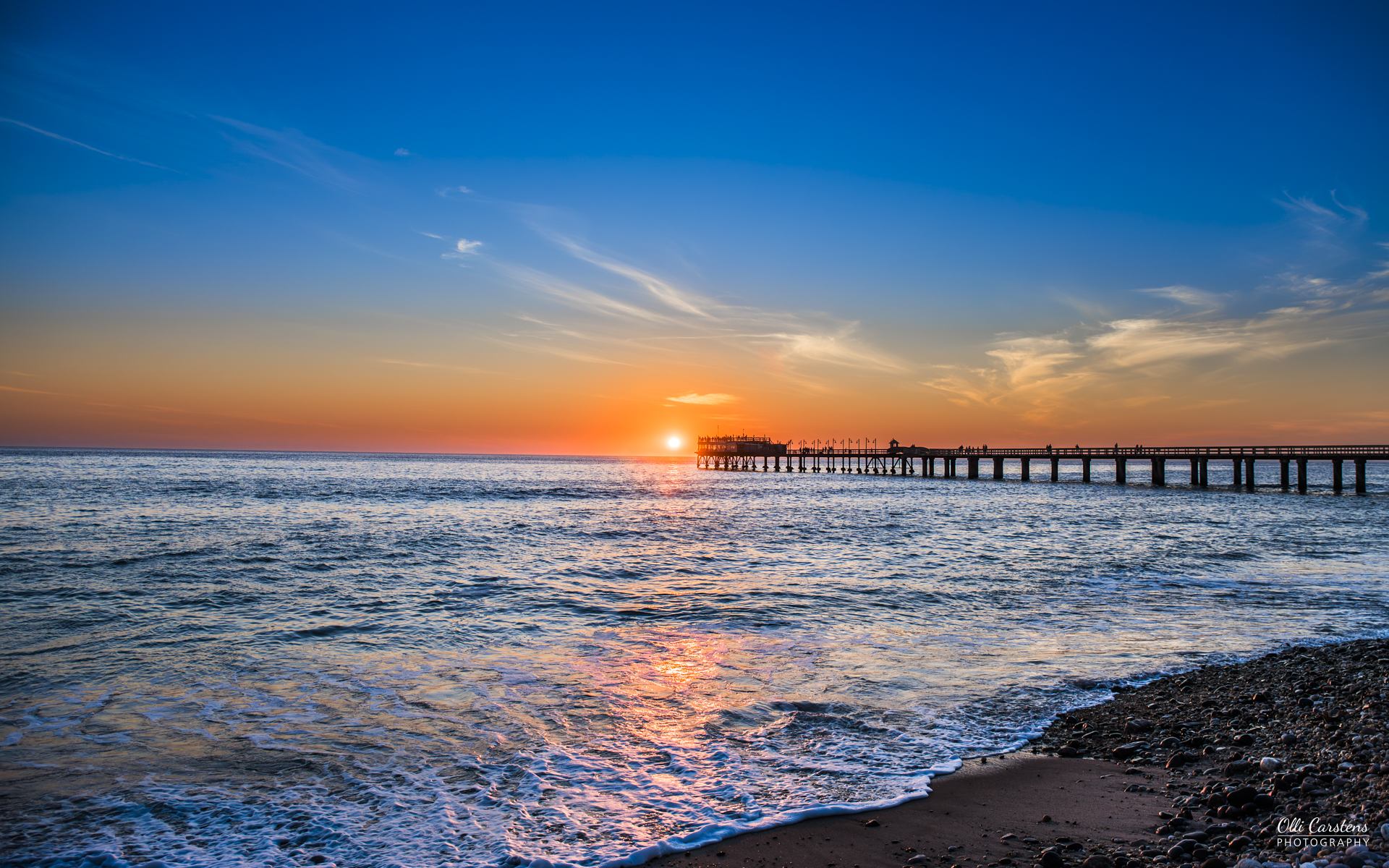 Swakopmund, Namibias Küstenstadt mit deutschem Flair Sonnenuntergang über dem Meer mit einem Pier im Vordergrund.
